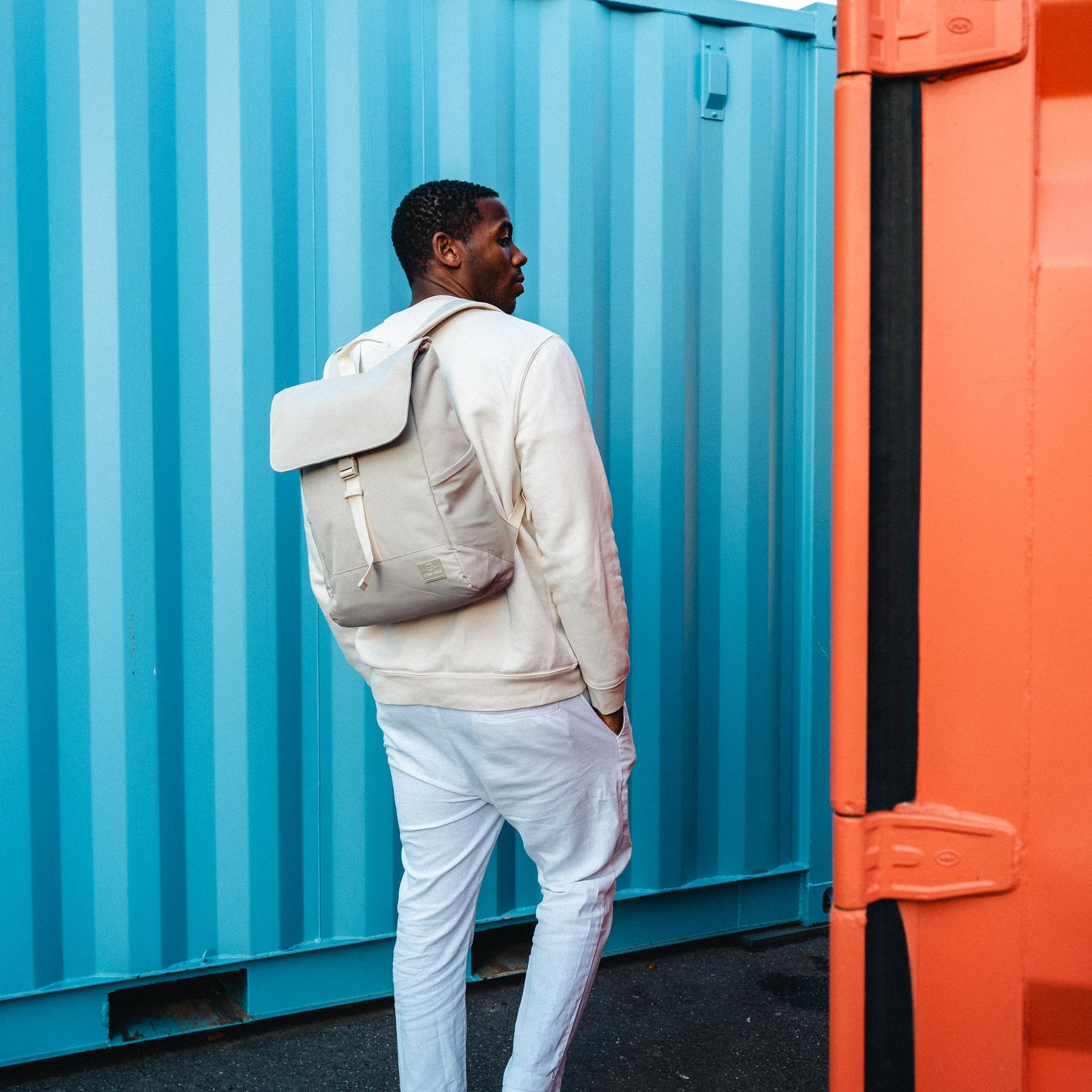 Mann trägt beigen Johnny Urban Rucksack 'Mika' vor blauem Container