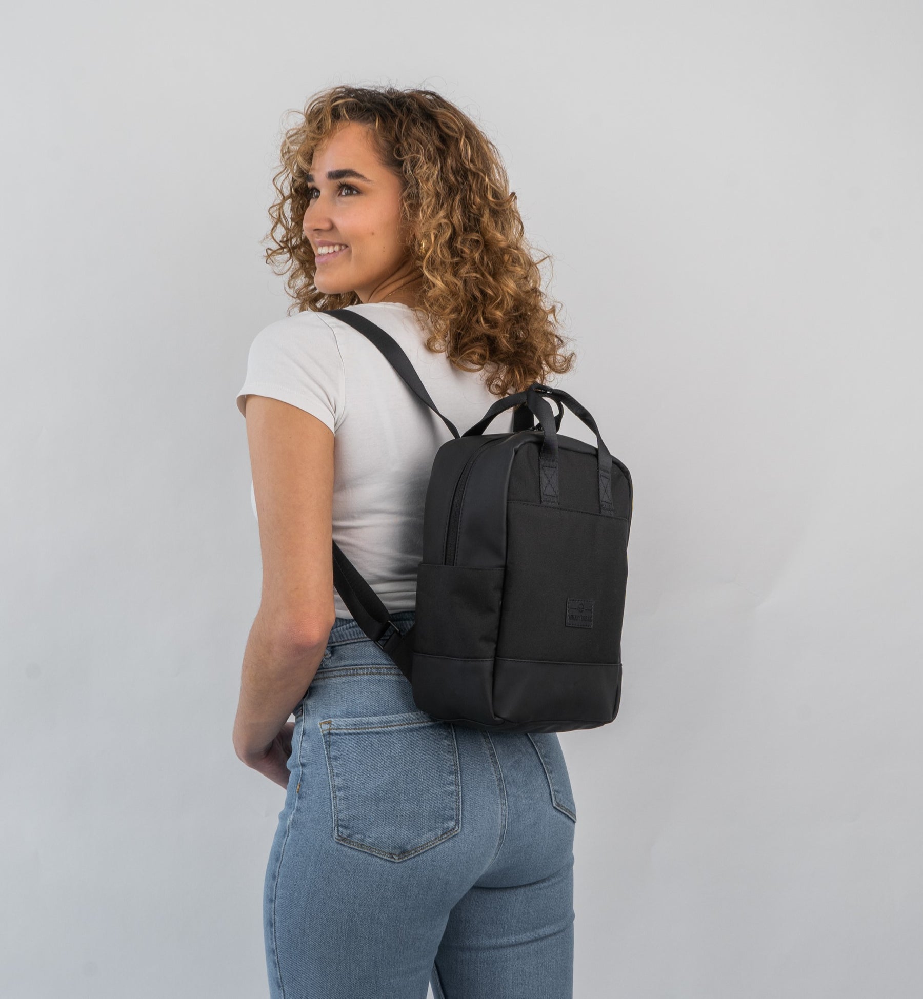 Frau mit lockigem Haar trägt schwarzen kleinen Rucksack 'Jona Small' von Johnny Urban