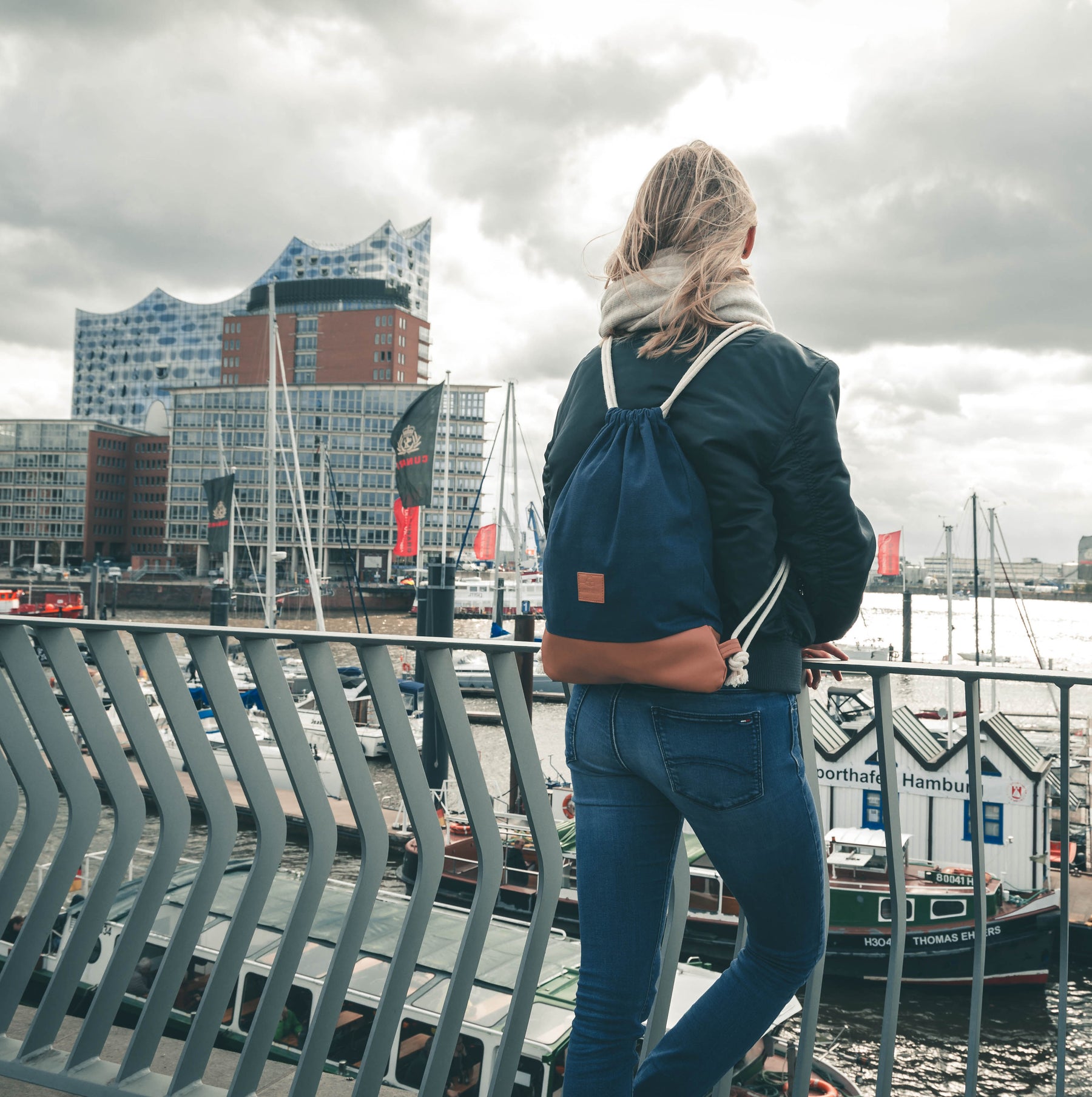 Frau mit Turnbeutel 'Luke' in Blau und Braun am Hafen mit Elbphilharmonie im Hintergrund