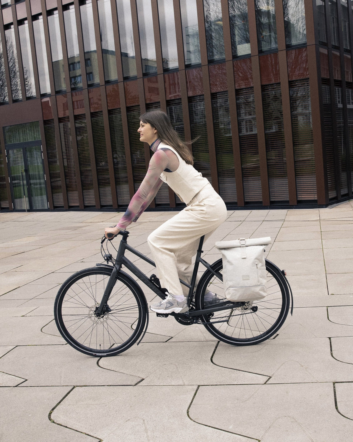 Frau fährt Fahrrad mit beigefarbenem Rolltop Rucksack 'Robin Medium' von Johnny Urban am Gepäckträger