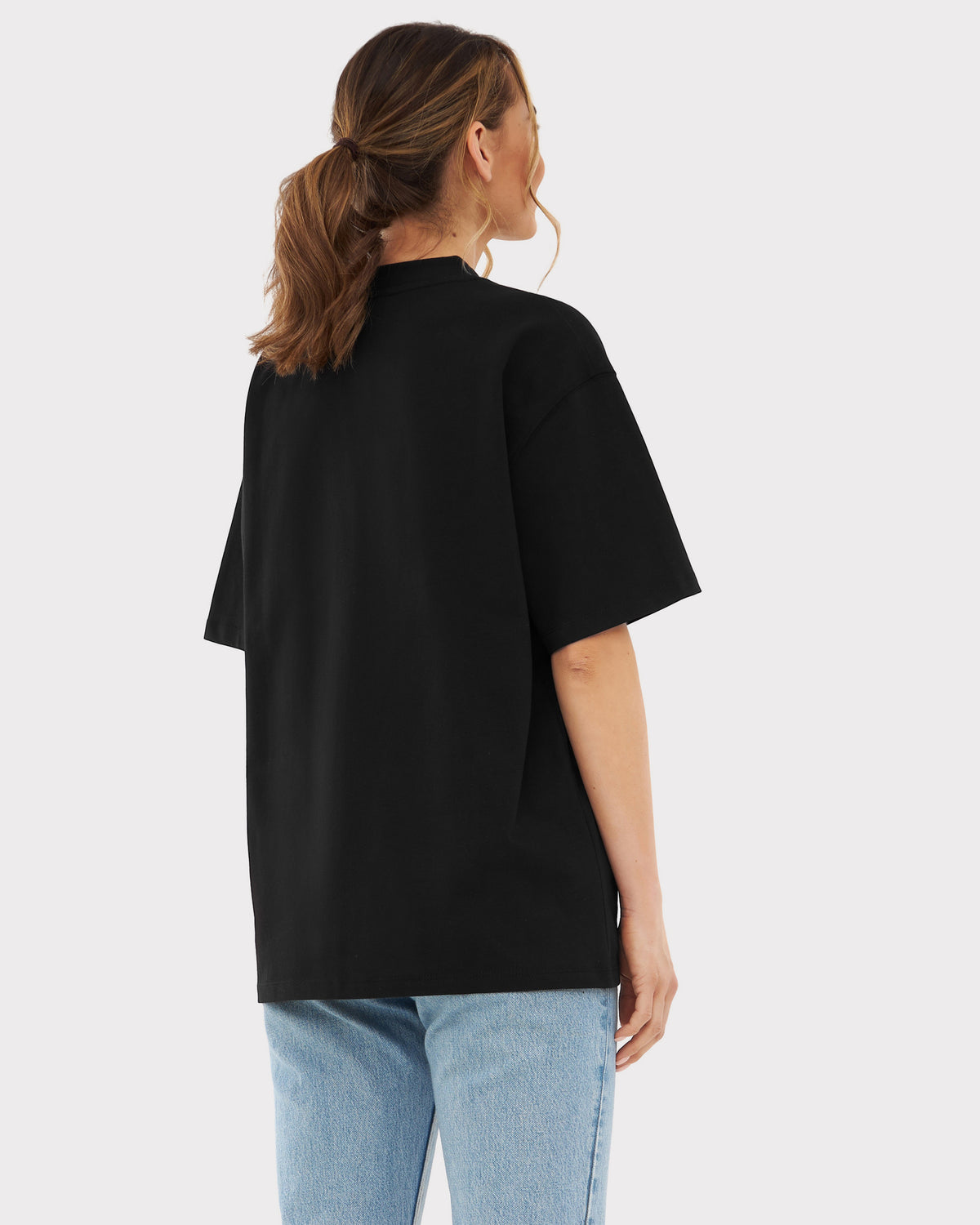 Frau trägt oversized schwarzes T-Shirt "Sammy Johnny Urban" von hinten, dazu blaue Jeans