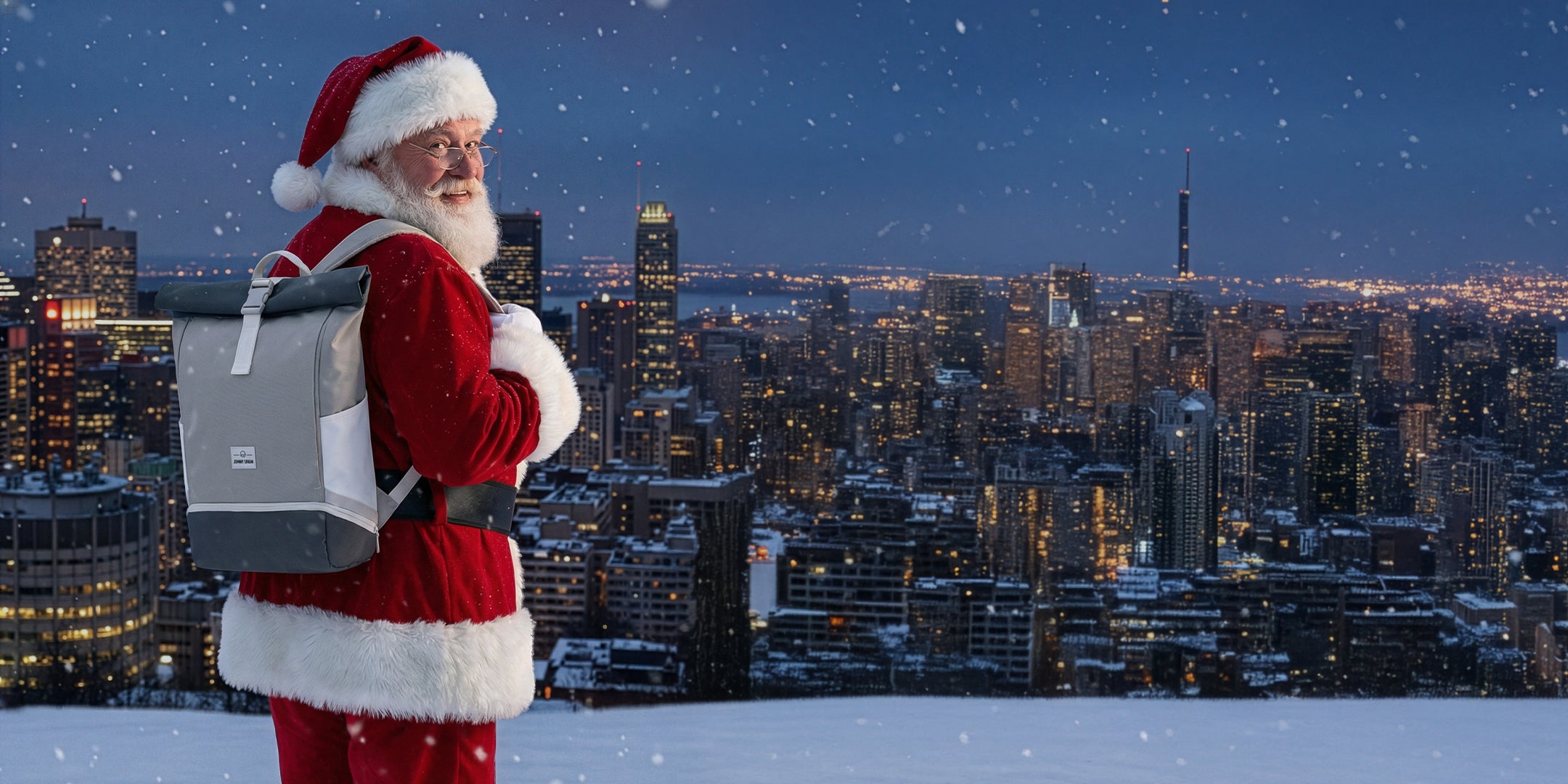Weihnachtsmann steht mit einem Rolltop aufem Rücken vor einer Skyline und es schneit.