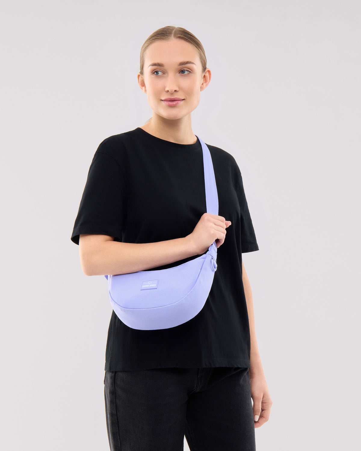 Frau trägt lila Half Moon Bag ‚Ally Small‘ von Johnny Urban über der Schulter, schwarze Kleidung