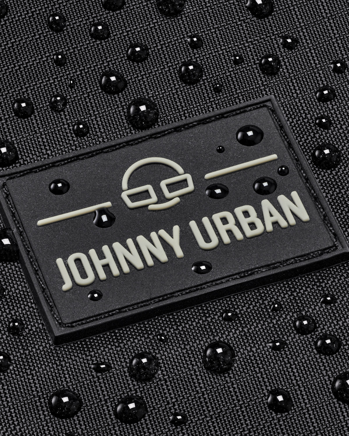 Nahe Aufnahme des Johnny Urban Logos auf einem wasserabweisenden schwarzen Gewebe mit Wassertropfen