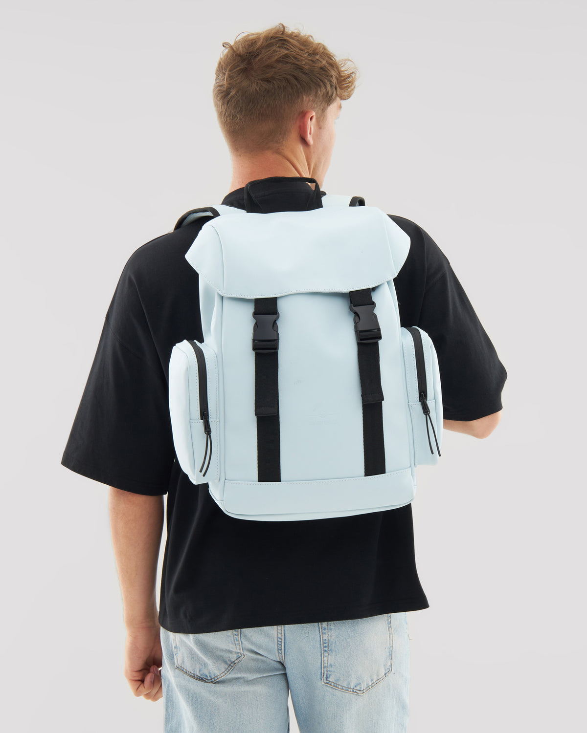 Hellblauer Rucksack 'Finley' mit zwei seitlichen Reißverschlusstaschen, getragen von einem Mann in schwarzem T-Shirt und hellen Jeans