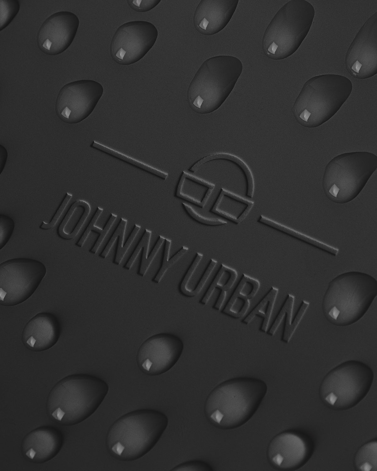Nahaufnahme des Johnny Urban Logos auf dem wasserabweisenden schwarzen Rucksack Finley mit Wasserperlen