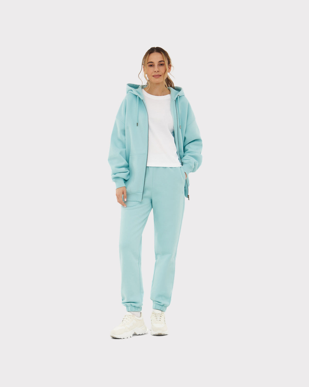 Frau trägt Jogginghose 'Owen' in Ice-Blau mit passendem Kapuzenpullover und weißem T-Shirt