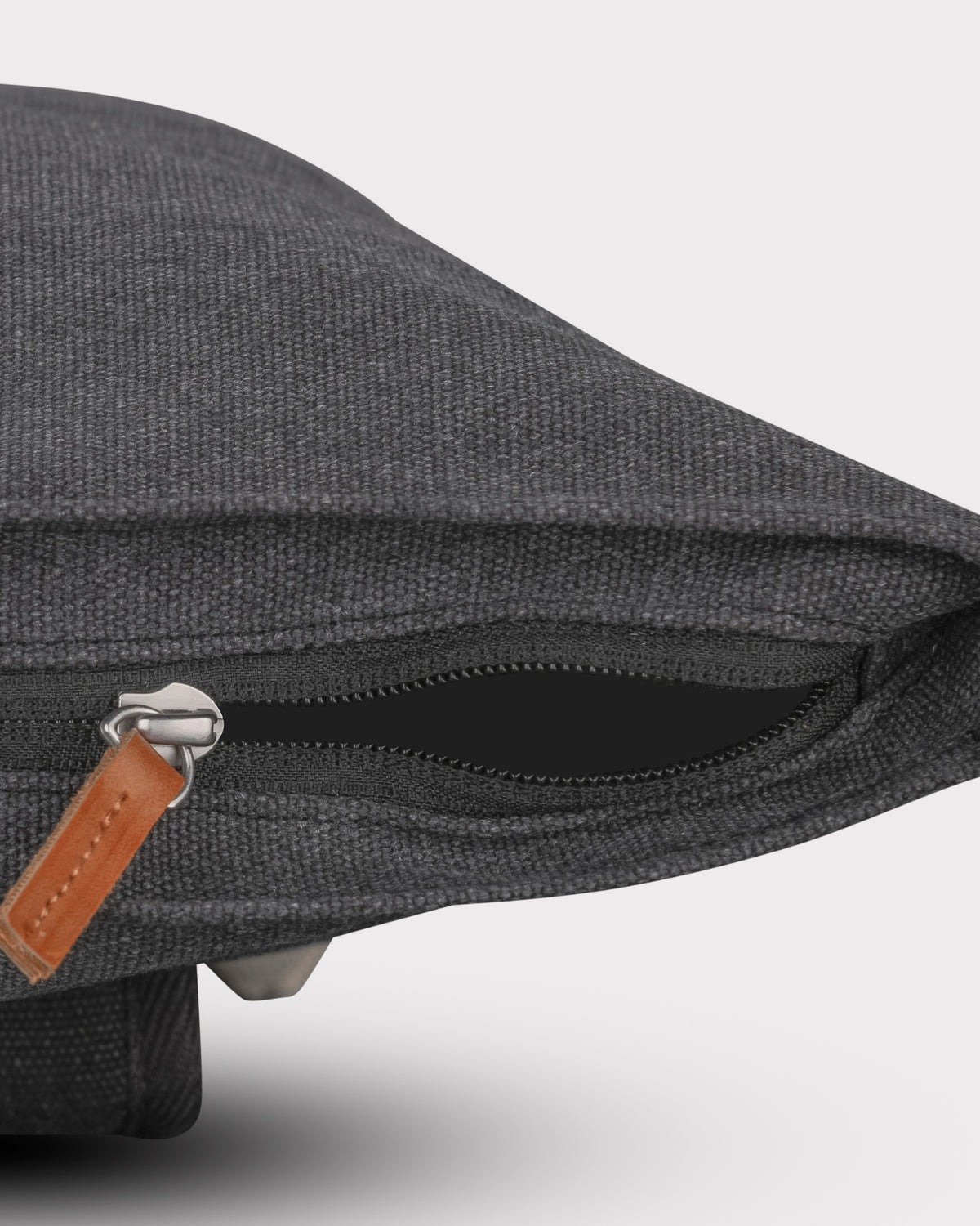 Detailansicht des schwarzen Canvas-Rolltop-Rucksacks 'Adam Medium' mit Reißverschluss und Lederanhänger