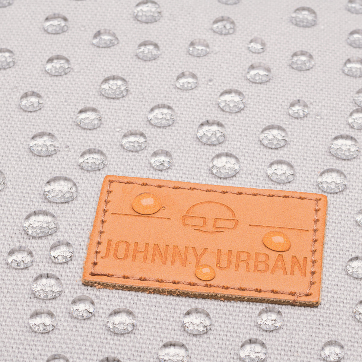 Wasserabweisendes graues Canvas-Material mit JOHNNY URBAN Lederetikett und Wassertropfen