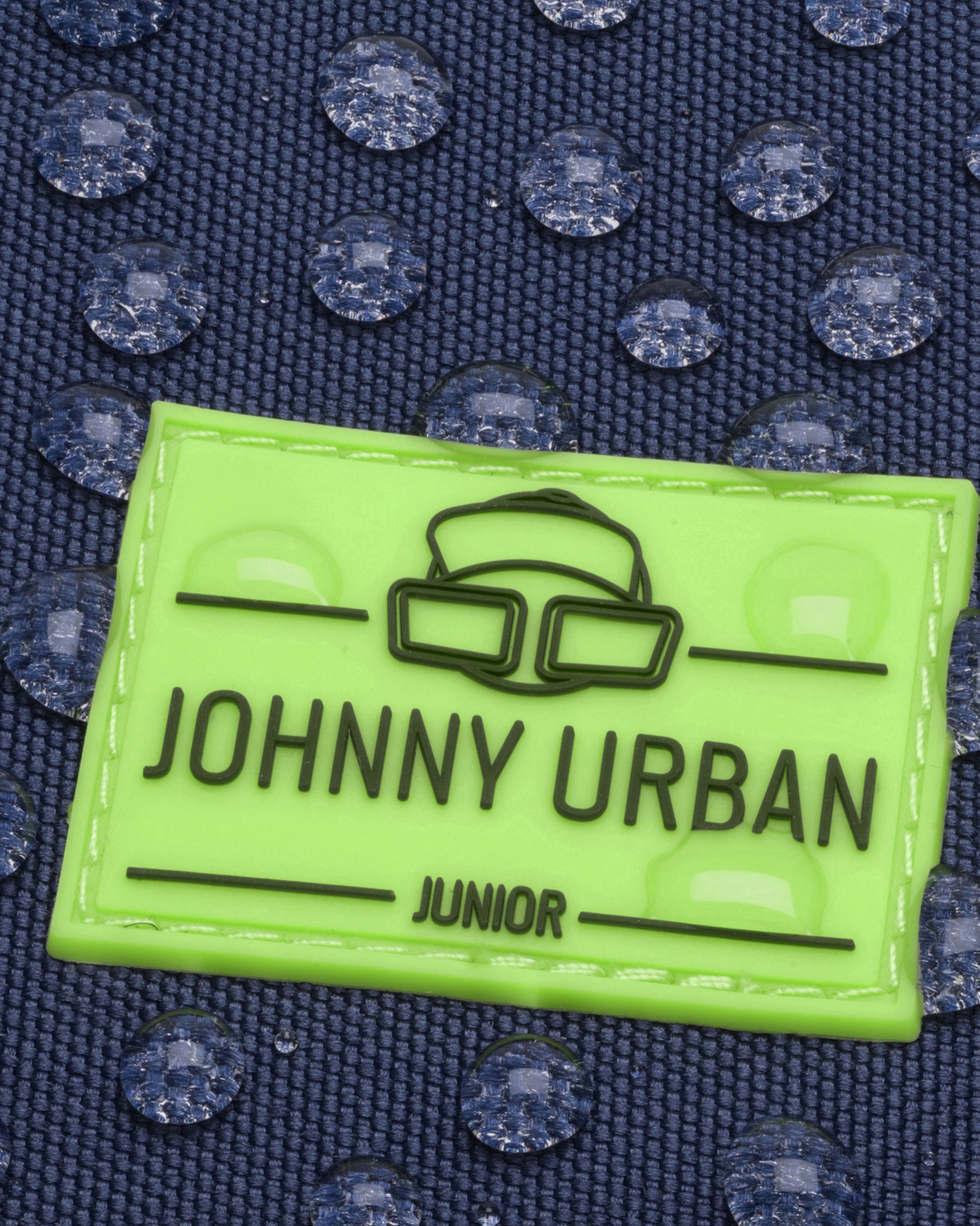 Nahe Aufnahme eines wasserabweisenden dunkelblauen Stoffes mit aufgenähtem neongrünem Johnny Urban Junior Logo-Patch