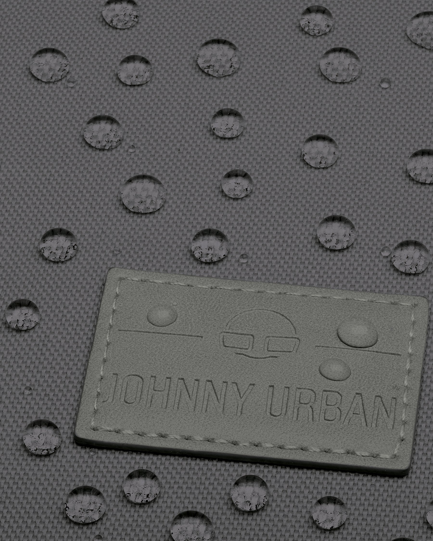 Nahaufnahme des dunkelgrauen Johnny Urban Rolltop Rucksacks mit wasserabweisender Textur und Wassertropfen