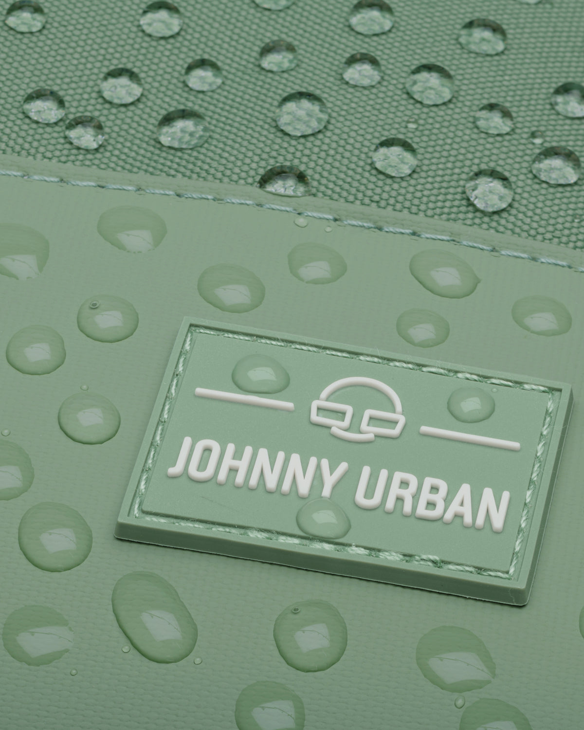 Nahaufnahme des Johnny Urban Logos auf dem wasserdichten Rucksack 'Mika' mit Wassertröpfchen